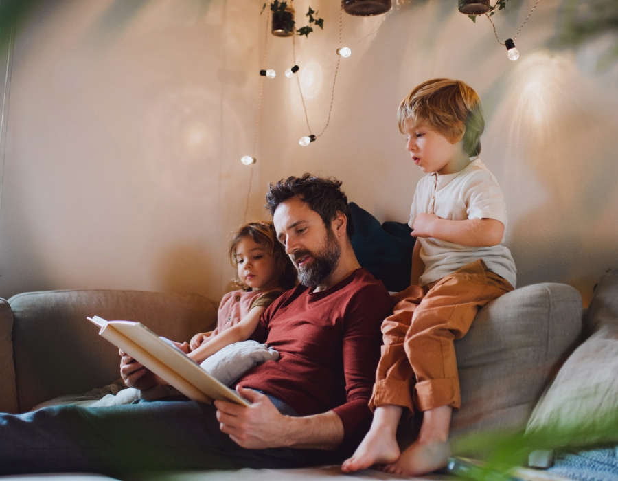 Vater sitzt mit seinen Kindern auf dem Sofa und liest etwas vor